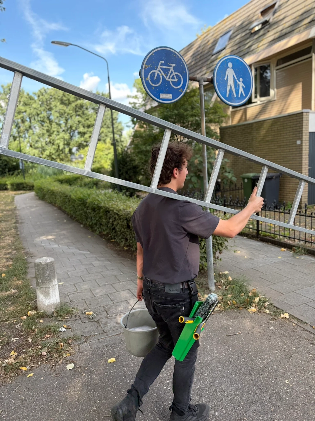 Teun loopt met ladder en emmer bij een woning